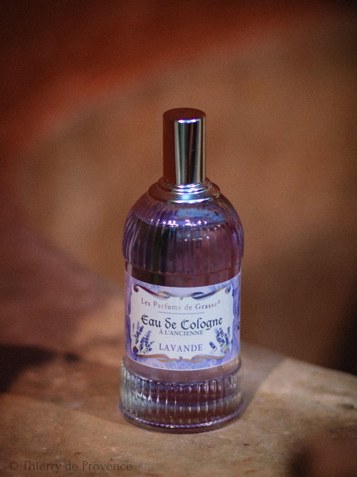 Laventeli-Eau de Cologne-pullo puiset taustat. Pullossa violetti etiketti, teksti "Eau de Cologne". Tunnelma on elegantti.